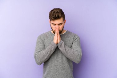 Mor arka planda izole edilmiş genç beyaz adam dua ediyor, bağlılık gösteriyor, dindar biri ilahi ilham arıyor..