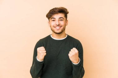 Genç Arap bir adam bej bir arka planda izole edilmiş tasasız ve heyecanlı tezahüratlar yapıyor. Zafer konsepti.