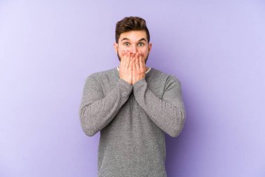 Mor arka planda izole edilmiş genç beyaz adam şok olmuş, ağzı ellerle kaplanmış, yeni bir şey keşfetmeye hevesli..