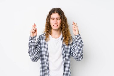 Genç uzun saçlı adam şans dilemek için parmaklarını çapraz yapıyor.