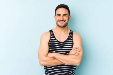 Mavi arka planda kendini güvende hisseden, kararlılıkla kollarını kavuşturan genç beyaz bir adam..