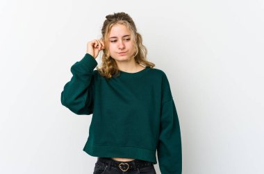 Beyaz arka plandaki genç beyaz kadın parmaklarıyla kulaklarını kapatıyor, gürültülü bir ortam yüzünden stresli ve çaresiz..