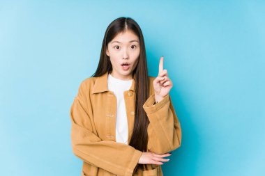 Mavi arka planda poz veren Çinli genç bir kadın harika bir fikri, yaratıcılık kavramını izole etmiş..