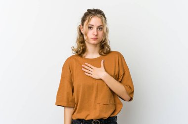 Beyaz arka planda genç beyaz kadın yemin ediyor, elini göğsüne koyuyor..