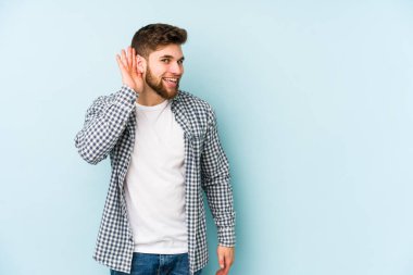 Mavi arka planda izole edilmiş genç beyaz adam bir dedikoduyu dinlemeye çalışıyor..