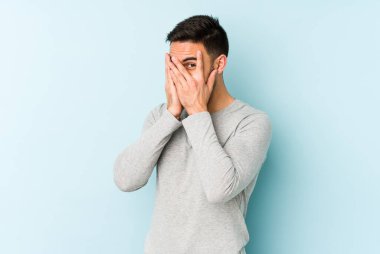 Kafkasyalı genç adam mavi arka planda izole edilmiş. Korkmuş ve gergin parmaklarıyla göz kırp..