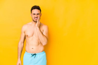 Sarı arka planda mayosu olan genç beyaz bir adam. Güçlü diş ağrısı ve diş ağrısı çeken beyaz bir adam..