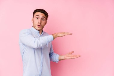 Pembe arka planda poz veren genç beyaz bir adam elleri arasında bir kopya alanı tutarken şok olmuş ve hayrete düşmüştü..