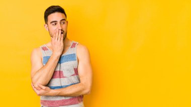 Sarı fırında izole edilmiş genç beyaz adam esniyor. Ağzı eliyle kapatan yorgun bir hareket sergiliyor..
