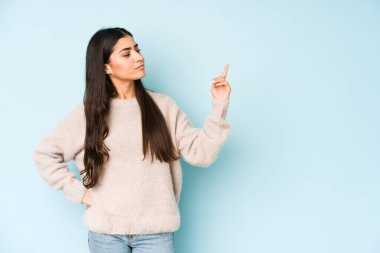 Mavi arka planda izole edilmiş genç Hintli kadın sanki seni davet ediyormuş gibi seni işaret ediyor..