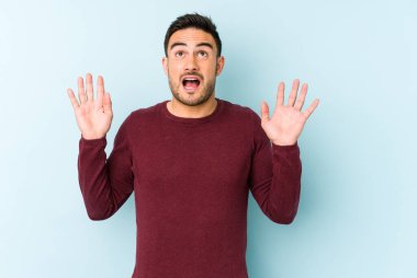 Kafkasyalı genç adam mavi arka planda izole edilmiş gökyüzüne haykırıyor, yukarı bakıyor, hayal kırıklığına uğramış..