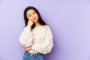 Mor bir arka planda izole edilmiş genç Çinli kadın üzgün ve düşünceli, fotokopi alanına bakıyor..