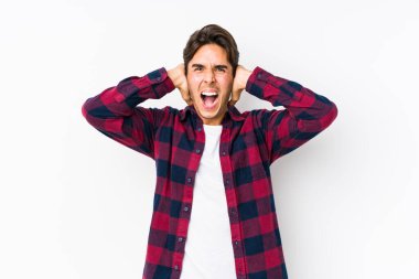 Pembe arka planda poz veren beyaz bir genç. Kulakları yalıtılmış, elleri sesi duymamaya çalışıyor..