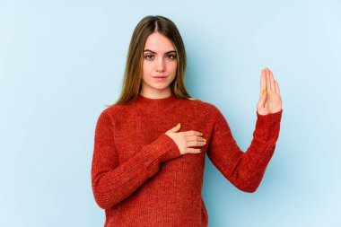 Beyaz bir kadın mavi arka planda izole edilmiş yemin ediyor, elini göğsüne koyuyor..
