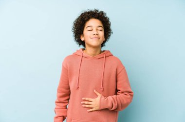 Afrikalı Amerikalı küçük çocuk karnına dokunuyor, nazikçe gülümsüyor, yemek yiyor ve tatmin oluyor..