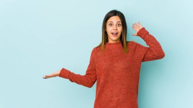 Mavi arka planda izole edilmiş genç bir kadın avuç içinde fotokopi alanı tutuyor, el üstünde tutuyor. Şaşırmış ve mutlu..