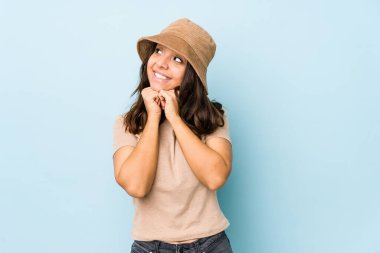 Genç, melez, yalnız bir kadın ellerini çenesinin altında tutuyor ve mutlu bir şekilde yan tarafa bakıyor..