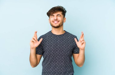 Genç Arap adam mavi arka planda izole edilmiş şans dilemek için şans diliyor.