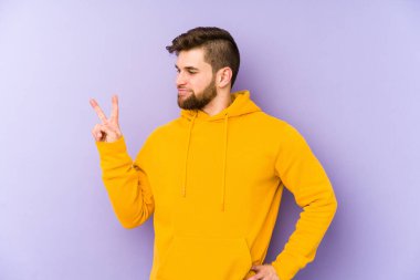 Mor arka planda izole edilmiş genç adam neşeli ve kaygısız parmakları olan bir barış sembolü gösteriyor..