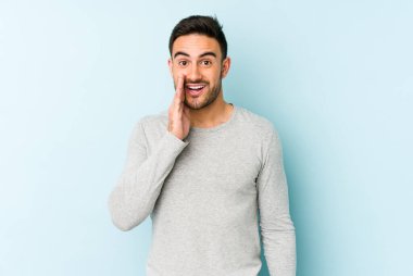 Mavi arka planda izole edilmiş genç beyaz adam yüksek sesle bağırıyor, gözleri açık ve elleri gergin tutuyor..