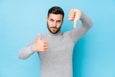 Mavi arka planda genç beyaz bir adam izole edilmiş, baş parmağını kaldırmıyor, zor seçim konsepti.