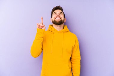 Mor arka planda izole genç adam iki ön parmağı da boş bir alan gösteriyor..