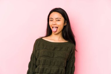 Genç Çinli bir kadın pembe arka planda izole edilmiş komik ve dostane bir dil uzatıyor..