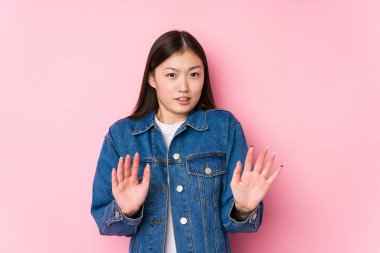 Pembe arka planda poz veren genç Çinli kadın dışlanmış, tiksinti belirtisi gösteren birini reddediyor..