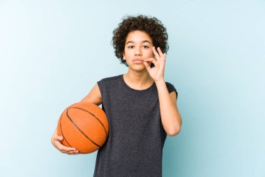 Çocuk basketbol oynuyor. Mavi arka planda izole edilmiş. Parmakları dudaklarında..