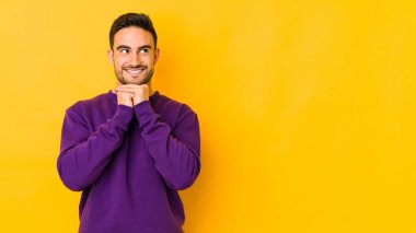 Sarı fırında izole edilmiş genç beyaz adam ellerini çenesinin altında tutuyor, mutlu bir şekilde yana bakıyor..