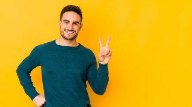 Sarı fırında izole edilmiş genç beyaz adam iki numarayı parmaklarıyla gösteriyor..