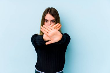 Mavi arka planda izole edilmiş genç beyaz bir kadın inkar jesti yapıyor.