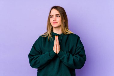 Mor arka planda izole edilmiş genç beyaz kadın dua ediyor, bağlılık gösteriyor, dindar biri ilahi ilham arıyor..