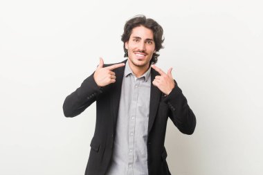 Beyaz arka planda genç bir iş adamı gülümsüyor, parmaklarını ağıza doğrultuyor..