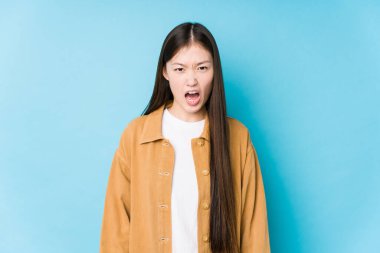 Mavi arka planda poz veren Çinli genç bir kadın çok sinirli ve agresif çığlıklar atıyor..