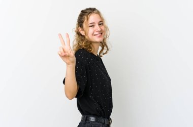 Beyaz arka plandaki genç beyaz kadın zafer işareti gösteriyor ve gülümsüyor..