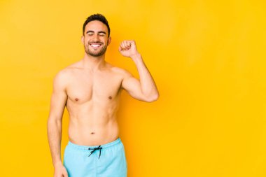 Sarı arka planda mayosu olan genç, beyaz bir adam zafer, tutku ve coşku dolu, neşeli bir ifadeyle beyaz bir adam..