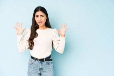 Genç Hintli kadın mavi arka planda izole edilmiş, gökyüzüne haykırıyor, yukarı bakıyor, hayal kırıklığına uğramış..