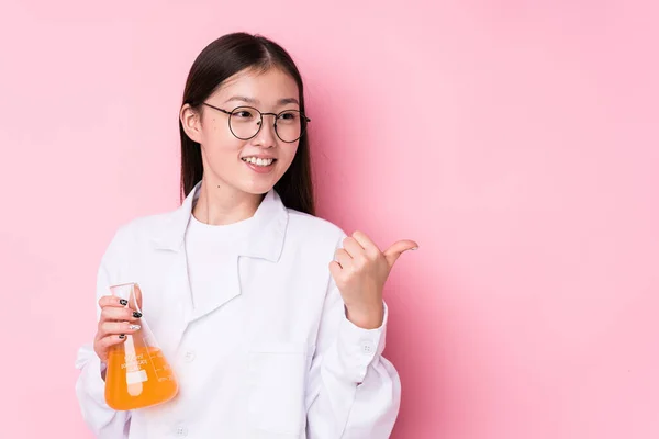 Young chinese scientific woman isolated points with thumb finger away, laughing and carefree.