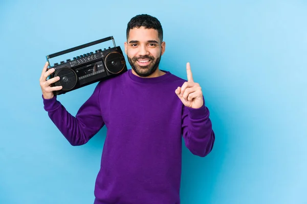 Young arabian man holding a radio cassette isolated Young arabian man listening music showing number one with finger.