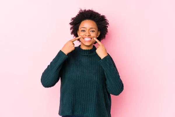 中年アフリカ系アメリカ人女性ピンクを背景に孤立した笑顔 口の中で指を指す — ストック写真