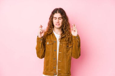 Genç uzun saçlı adam şans dilemek için parmaklarını çapraz yapıyor.