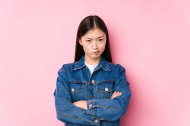 Pembe arka planda poz veren Çinli genç bir kadın hoşnutsuzca somurtan bir yüz, kollarını kavuşturuyor..