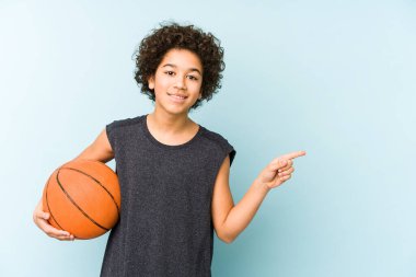 Basketbol oynayan çocuk mavi arka planda izole edilmiş gülümseyen ve işaret eden boş alanda bir şey gösteriyor..