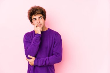 Pembe arka planda genç beyaz bir adam izole edilmiş, rahat bir şekilde fotokopi odasına bakan bir şey düşünüyor..