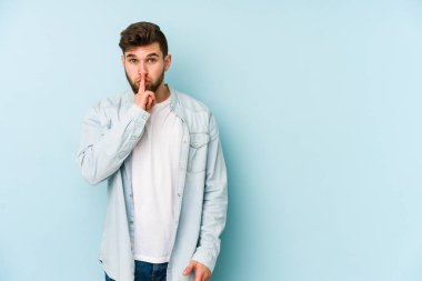 Mavi arka planda izole edilmiş genç beyaz bir adam ya sır saklıyor ya da sessizlik istiyor..