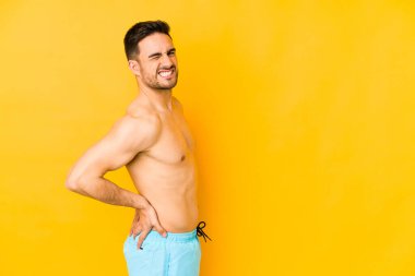 Sarı arka planda mayosu olan genç, beyaz bir adam sırt ağrısı çeken beyaz bir adam..