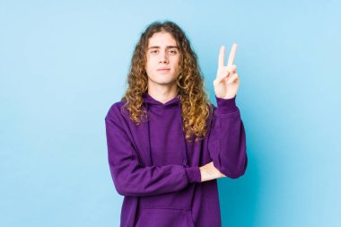 Uzun saçlı adam yalnız poz veriyor. İki numarayı parmaklarıyla gösteriyor..