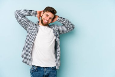 Mavi arka planda izole edilmiş genç beyaz adam kollarını uzatıyor, rahat bir konumda..