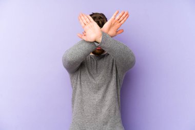 Mor arka planda izole genç beyaz adam iki kolu çapraz tutuyor, inkar kavramı.